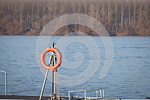 Orange lifebuoy hanging on a pier by a river next to the sea. This lifebuoy is used to protect people in case of drowning