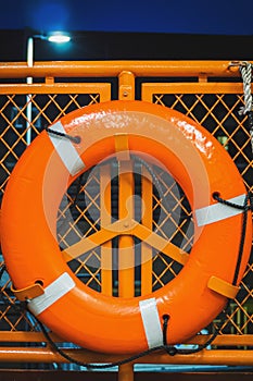 Orange lifebuoy hanging on a safety guardrail of a ferry boat at night sea