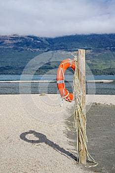 An orange lifebuoy hanging on a wooden pole on a beach near a lake shore
