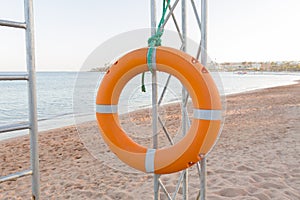 Orange lifebuoy on lifeguard tower on blue sky and beach background