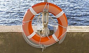 Orange lifebuoy and old rope hanging by the river