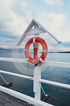 Orange lifebuoy on the pier beach by sea. Safety equipment for rescuing people on seashore. Blue sky and azure sea