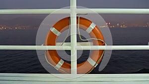 Orange lifebuoy at the railing of a cruise ship deck on dusk