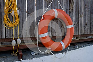 an orange lifebuoy and a rope with buoys hang on a wooden fence. Rescue equipment for emergency on water.