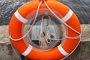 Orange lifebuoy with rope on a pier near the water