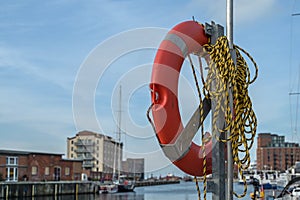 Orange Lifebuoy with rope on the quay in the old port of Wismar on the Baltic Sea, blue sky, copy space