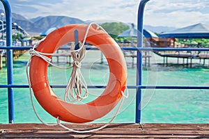 Orange lifebuoy with rope on wooden pier near sea.