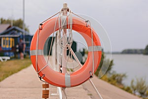 The orange lifebuoy is tied to a fence on the river pier. frontal view