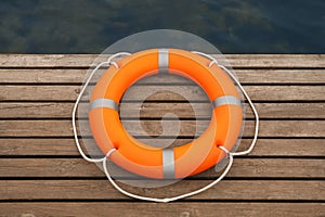 Orange lifebuoy on wooden pier near water. Rescue equipment