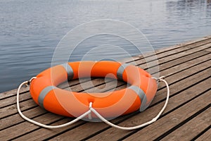 Orange lifebuoy on wooden pier near water. Rescue equipment