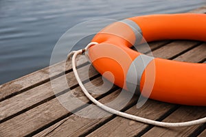 Orange lifebuoy on wooden pier near water. Rescue equipment