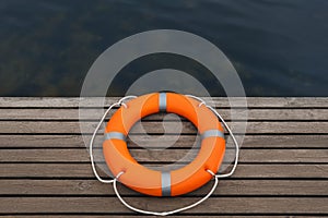 Orange lifebuoy on wooden pier near water. Rescue equipment