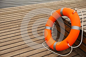 Orange lifebuoy on wooden pier, space for text. Rescue equipment