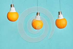 Orange in a light bulb is suspended from a rope. turquoise background. creative concept