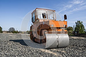 Orange light Vibration roller compactor standing on a stones at road construction and repairing asphalt pavement works