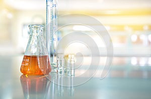 orange liquid in glass flask with cylinder vial in chemical science laboratory background