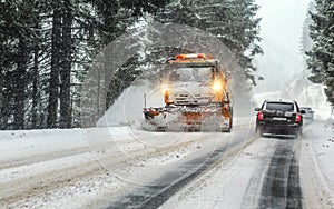 Orange maintenance plough truck on forest road in snowstorm blizzard. Roads in this