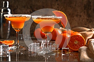 Orange margarita cocktail with alcoholic and ice cubes and fruits orange background for refreshing summer concept