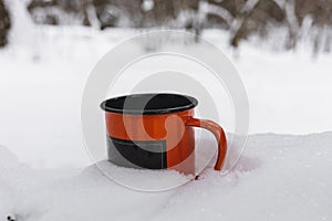 Orange metal mug with beverage standing in snow. Tourist winter picnic concept