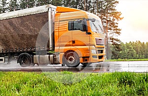 orange modern truck with a semi-trailer is driving on a wet road in the rain. Slippery road, tire grip, trucking