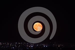 Orange moon rising on night sky above city lights