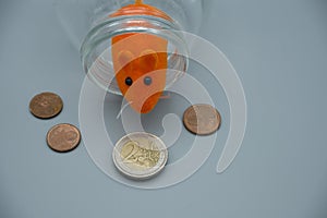 An orange mouse in a glass jar with euro coins. Concept of erosion of earning