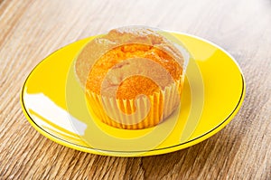 Orange muffin in yellow saucer on wooden table