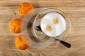Orange muffins, glass with latte-macchiato, spoon on saucer on wooden table. Top view