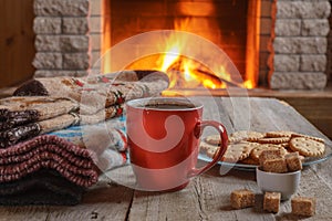 Orange mug for tea or coffee; wool things near cozy fireplace.