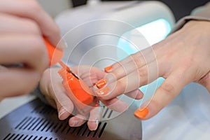 Orange nail varnish being applied to woman's finger nails