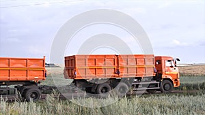 Orange, new ruck with trailer moving on country road on green and yellow field background. Scene. Lorry with a trailer photo