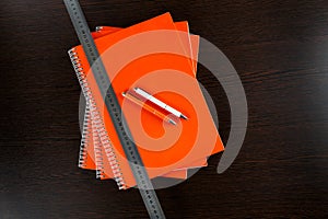 Orange notebooks lying on a dark brown wooden table with an orange and white pens and measure tape