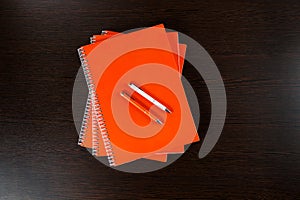 Orange notebooks lying on a dark brown wooden table with an orange and white pens