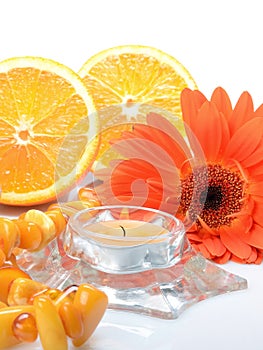 Orange objects on a white background: an orange gerbera flower, an amber beads and candle - still life