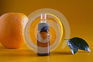 Orange organic aromatic oil in a glass bottle with a pipette next to a fresh orange