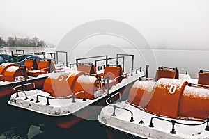 Orange paddleboats by the pier on a calm lake captured on a foggy winter day