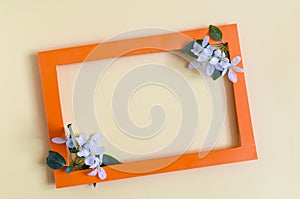 Orange paper frame decorated with white flowers and green leaves on a white background. Flat ley bright orange