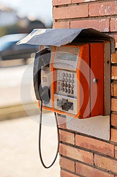 an orange pay phone hanging on a brick wall near a road