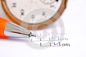 orange pen on a  sheet of white paper with printed financial numerical data table with columns with clock on back Concept for