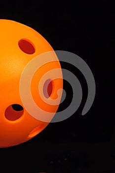 Orange Pickleball emerging from left on Black background.