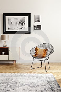 Orange pillow on a black, industrial net chair by a white wall with gallery of mock-up pictures in an elegant living room interior