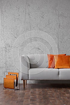 Orange pillows on grey settee in living room interior with concrete wall and wooden floor. Real photo photo