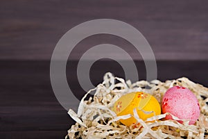 Orange and pink Easter eggs in straw on dark wooden background