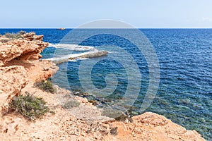 Orange-pink rocky coast with rare plants, water changes color depending on depth, clear sky, summer day, Ibiza, Balearic Islands,