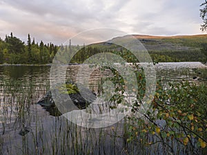 Orange pink sunset over lake Sjabatjakjaure in Parte in Sweden Lapland. Mountains, birch trees, spruce forest, rock boulders and