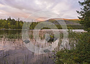 Orange pink sunset over lake Sjabatjakjaure in Parte in Sweden Lapland. Mountains, birch trees, spruce forest, rock boulders and g photo