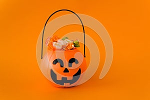 Orange plastic candy basket in the shape of a pumpkin jackolantern on a orange background. Place for your text, layout
