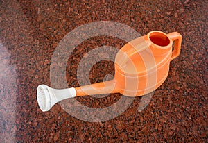 Orange plastic watering can on granito tile floor photo