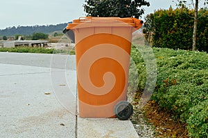 An orange plastic wheeled recycling rubbish bin beside the road