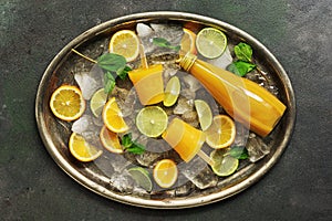 Orange popsicles, orange juice in a bottle, sliced citrus fruits, mint leaves and crushed ice on a metal vintage tray. Summer